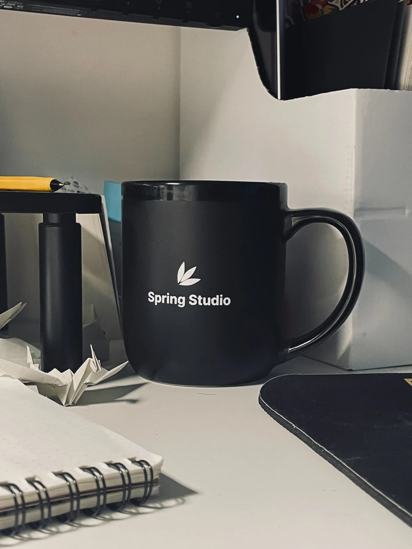 A Spring Studio mug on a desk beside a notebook