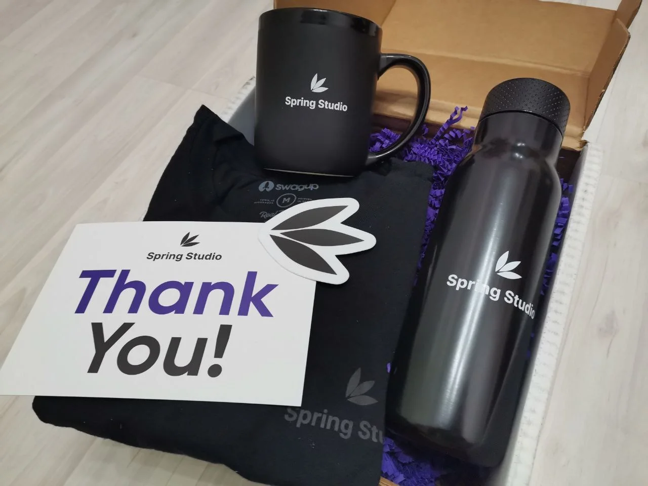 A Spring Studio welcome pack with a mug, shirt, bottle, and thank-you note